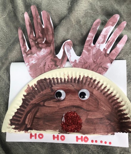 A paper plate folded in two and designed as a reindeer, with cut out paper hands as antlers.